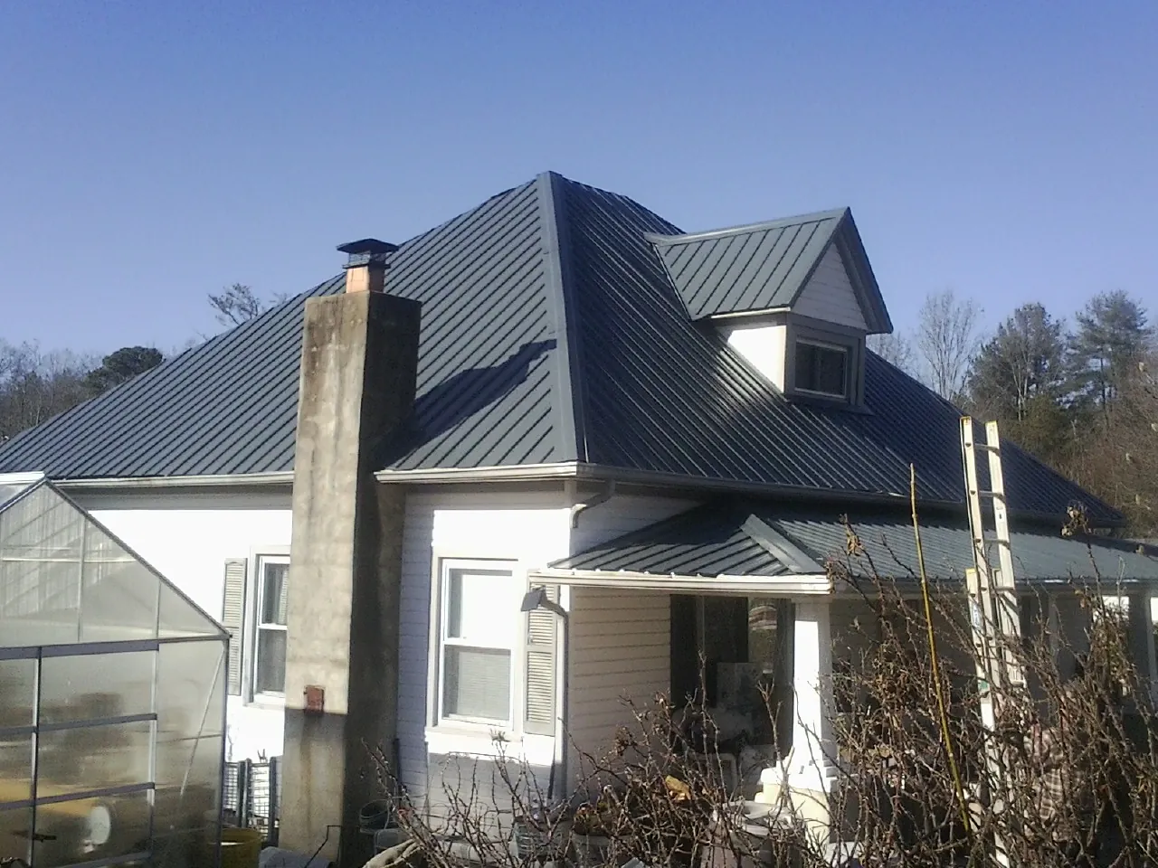 Dark blue standing seam metal roof on a white farmhouse with dormer — Slate & Tile Roof Repair by Roofing Brothers in Lake Hamilton