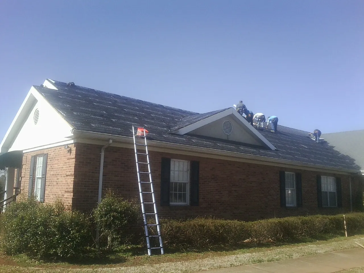 Crew tearing shingles off a brick ranch roof with a ladder set — Metal Roof Repair work by our crew in Lake Hamilton