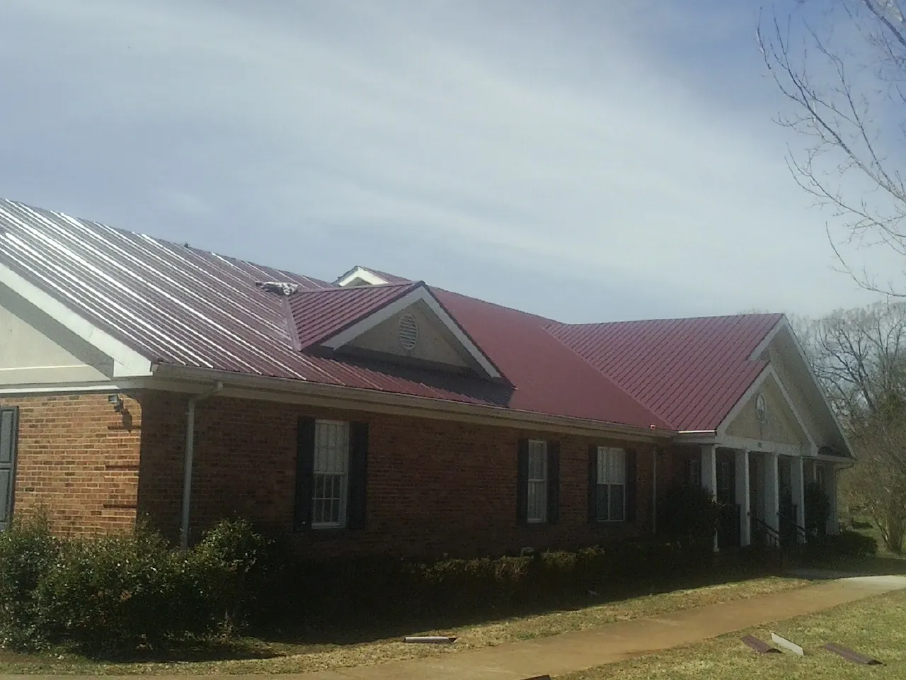 Red metal roof with gabled entries on a long brick building, from a Hail Damage Roof Repair job in Lake Hamilton