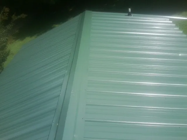 New green metal panels meeting at the ridge of a roof — Flat Roof Repair work by our crew in Lake Hamilton