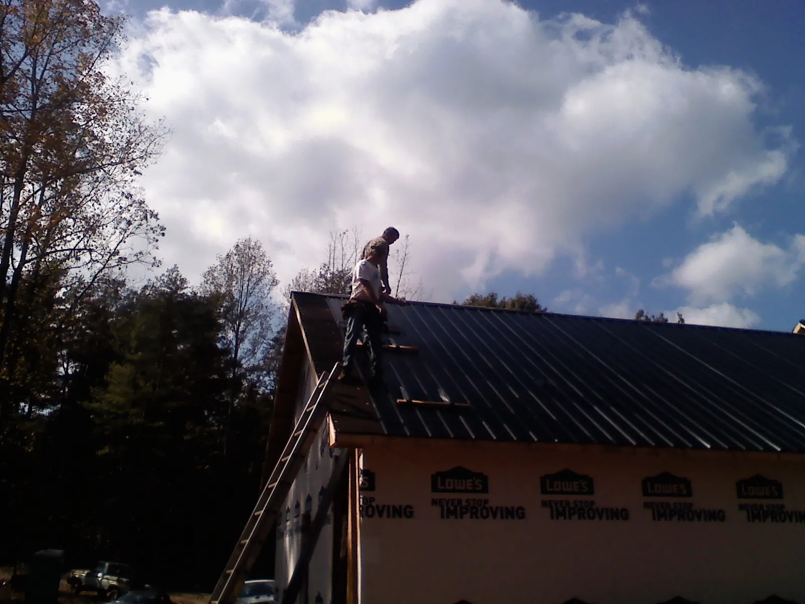 Roofer fastening dark metal panels high against a cloudy sky, from a Roof Inspection job in Lake Hamilton