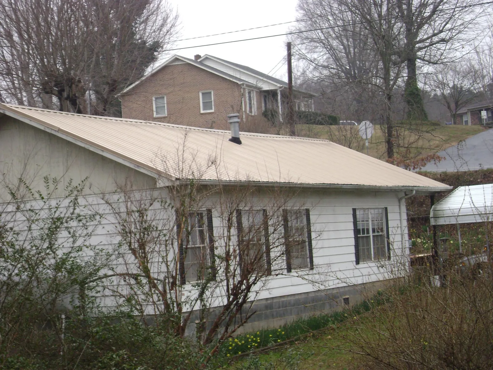 Tan metal roof on a white sided house set into a hillside — Commercial Roofing by Roofing Brothers in Lake Hamilton