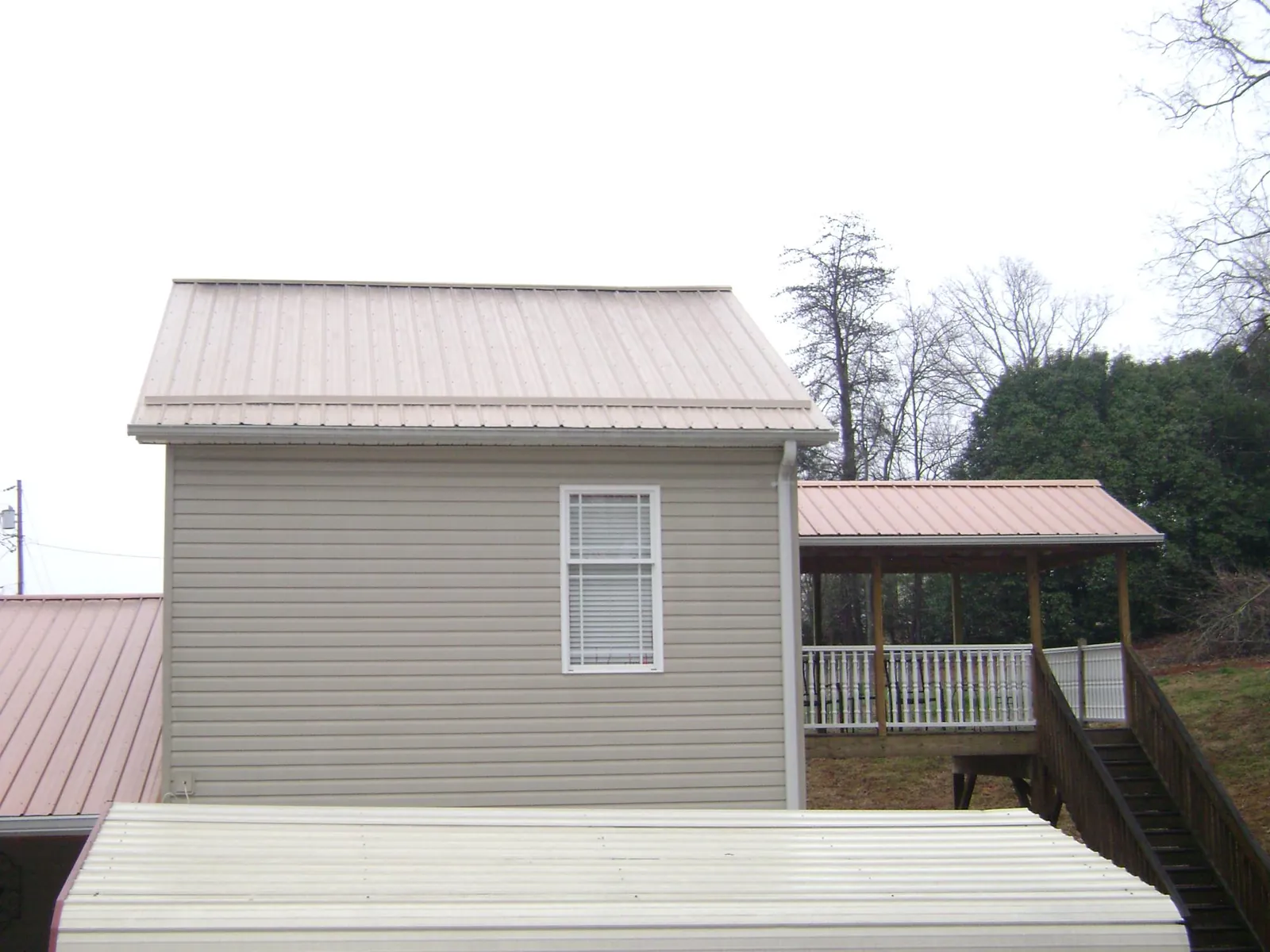 Tan metal roofs on a two story addition and attached porch, from a Roof Replacement job in Lake Hamilton